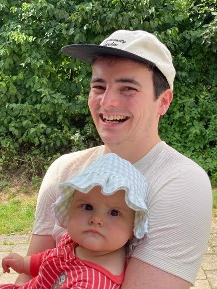 Xander's smiling while holding a grumpy baby.