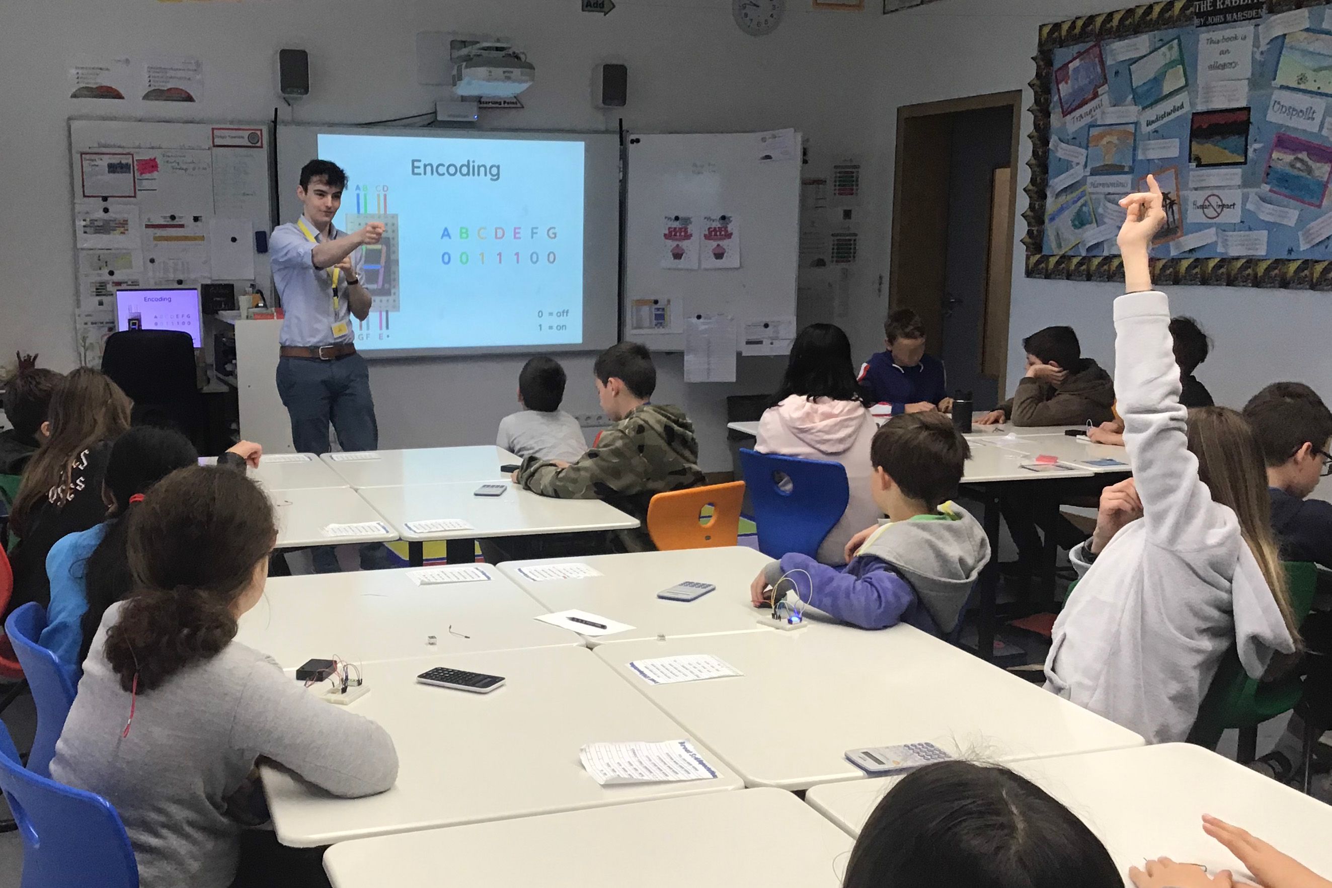 Xander stands at the front of a classroom and answers a question while leading a workshop on digital encoding.